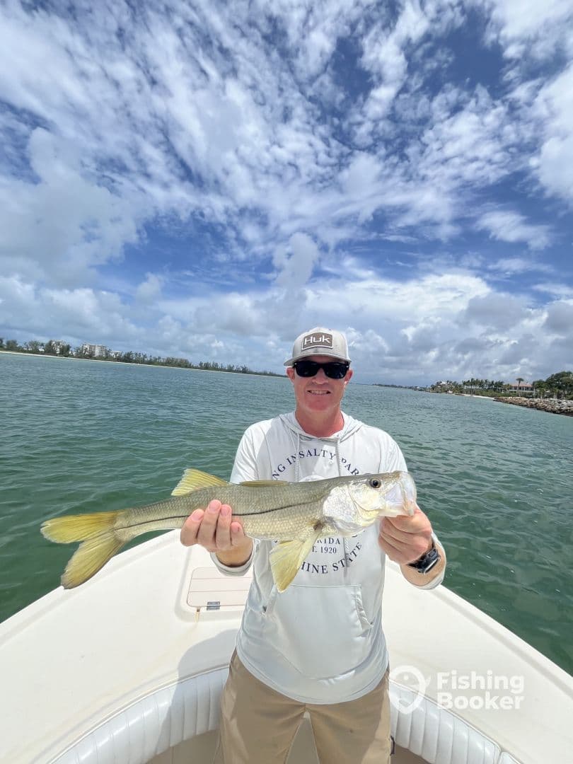 An angler proudly displaying a Snook caught while fishing from a boat in a scenic coastal environment.