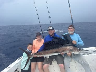 A family proudly displays a large Sailfish caught during their offshore fishing trip, showcasing the excitement of deep-sea fishing.