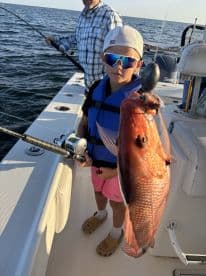 A young angler proudly displaying a Red Snapper while fishing on a boat, showcasing a fun family outing on the water.