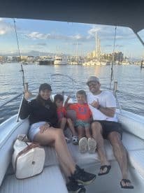 A family enjoying a relaxing moment on the boat, showcasing a scenic marina backdrop with multiple yachts.