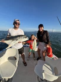 A family enjoying a successful fishing trip, showcasing their catch of a large fish and a smaller one on a boat in a sunny environment.