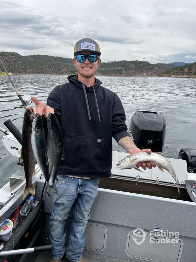 Angler displaying a catch of multiple fish, including a large trout, while fishing on a scenic lake surrounded by mountains.