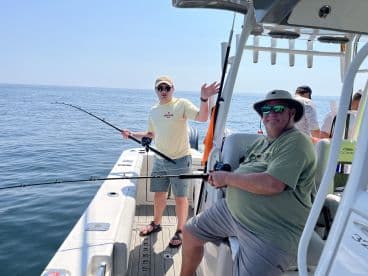 Two anglers enjoying a day of fishing on a boat, with one actively reeling in a line while the other poses for the camera.