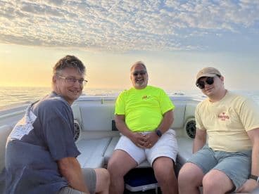 Three anglers relaxing inside a boat, enjoying a calm sunset on the water, showcasing a comfortable seating area.
