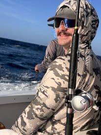 Angler enjoying a fishing trip on a boat, equipped with a fishing rod and wearing protective gear against the sun.