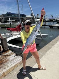 Excited angler displaying a large King Mackerel at the marina, showcasing a successful fishing trip.