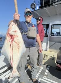 An angler proudly displaying a large Halibut aboard a fishing charter in open waters, showcasing a successful catch.