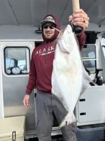 Angler proudly displaying a large Halibut aboard a fishing charter in Alaska.