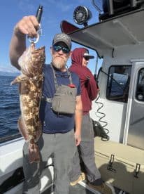An angler proudly displaying a large Rockfish while fishing on a boat in open waters.
