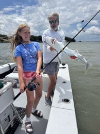A young angler is excitedly holding a caught shark while fishing on a boat, showcasing a memorable moment during a family fishing trip.