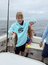 A young angler proudly displaying a Black Sea Bass and a Red Snapper while fishing on a boat, showcasing a successful day on the water.