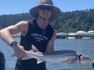 Angler holding a Sturgeon while fishing on a sunny day, showcasing a successful catch near a scenic waterfront.