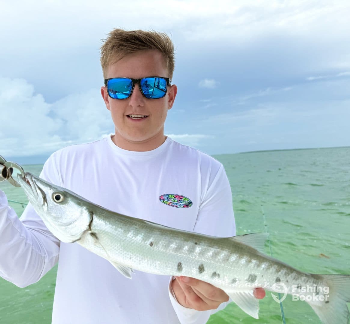 A young angler proudly displaying a Barracuda while fishing in clear waters, showcasing a successful day on the water.