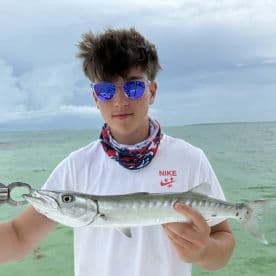 Young angler proudly holding a Barracuda while fishing in clear waters, showcasing a successful catch during a coastal trip.