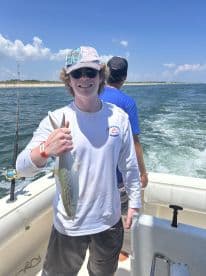 A young angler proudly displaying a Spanish Mackerel while fishing on a boat, enjoying a sunny day on the water.
