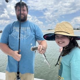 A young girl and her father proudly display a small shark caught during their fishing trip, enjoying a sunny day on the water.