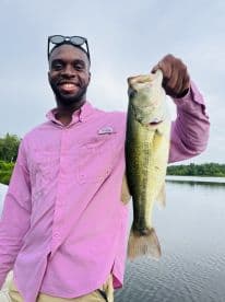 An angler proudly displaying a large Largemouth Bass while fishing on a serene lake.