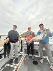 A family of three proudly displaying their catch of salmon on a fishing charter, showcasing a successful day on the water.