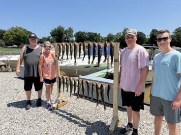 A group of four anglers proudly displaying their catch of fish on a board at the marina, showcasing a successful day of fishing.