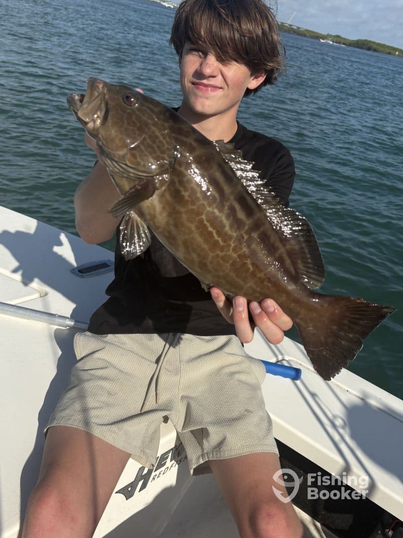 A young angler proudly displaying a large Grouper while fishing on a boat, showcasing a successful day on the water.