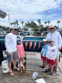 A family poses proudly in front of a catch board displaying several Red Snapper after a successful fishing trip.