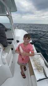 Young angler proudly holding a Red Snapper on a fishing boat, showcasing a successful catch during a day at sea.