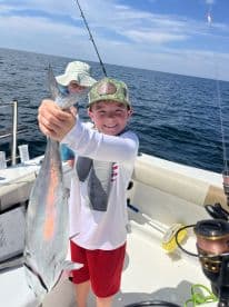 A young angler proudly displaying a fish while fishing on a boat in open waters, showcasing a fun day out on the sea.