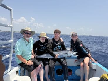 A family of four proudly displaying a large fish on a fishing boat, enjoying a sunny day on the water.