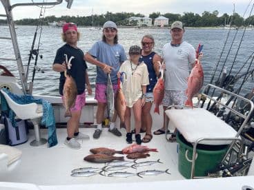 A family group proudly displaying their catch of colorful Snapper and other fish on a fishing charter in a coastal setting.