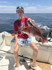 Young angler proudly holding a large Red Snapper while fishing on a sunny day.
