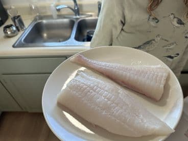 A young angler displaying freshly filleted fish in a kitchen setting, showcasing the catch from a recent fishing trip.