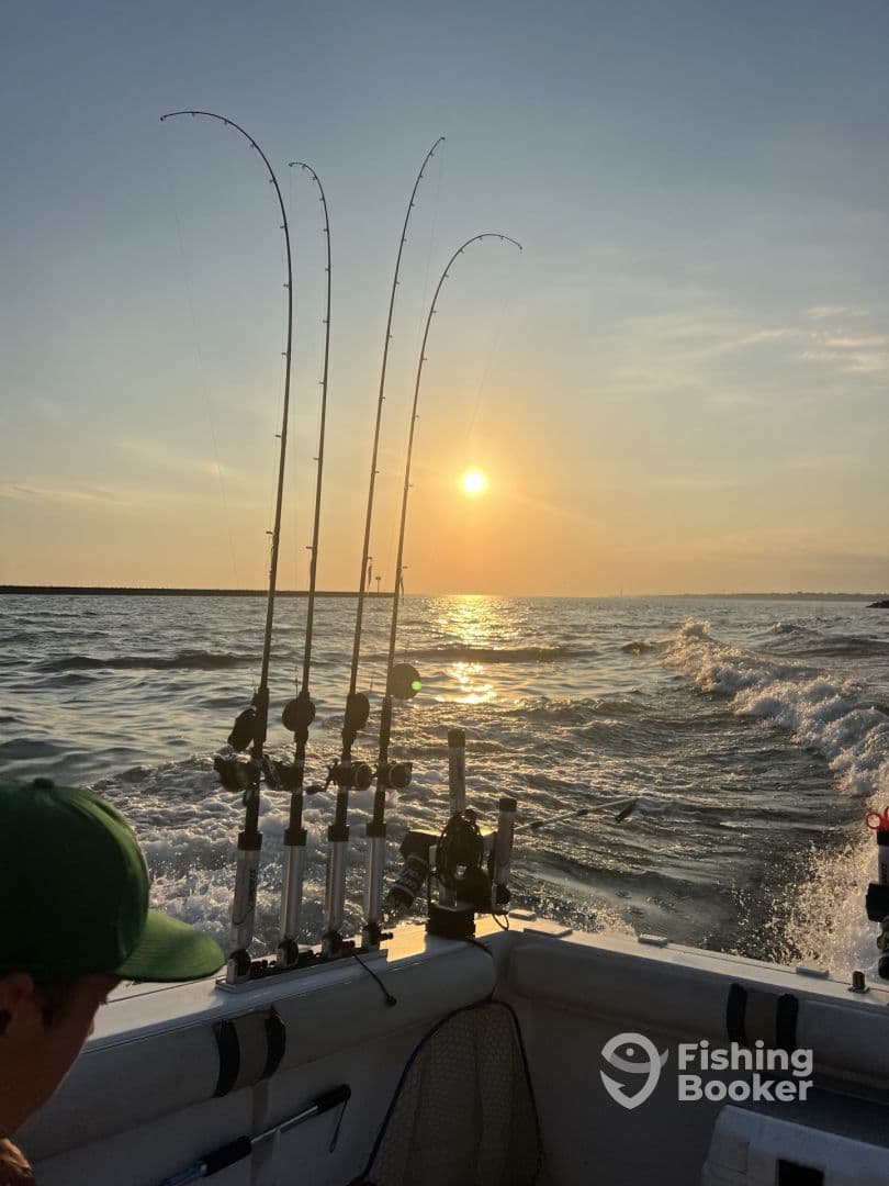 A young angler is seated inside a boat, with fishing rods set up against a stunning sunset backdrop on the water.
