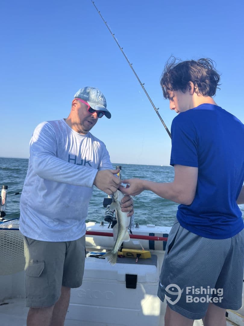 A young angler and an adult are working together to handle a freshly caught fish on a boat, showcasing a successful fishing experience.