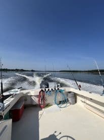 View from the helm of a fishing boat, showcasing fishing rods and equipment while cruising on calm waters.