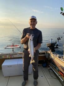An angler proudly displays a freshly caught trout while fishing on a calm lake, showcasing a beautiful morning fishing experience.