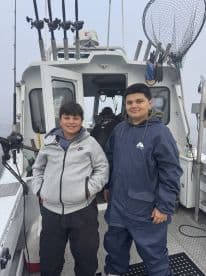 Two young anglers posing inside the boat, showcasing the interior setup with fishing gear visible in the background.