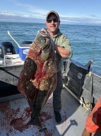 Angler proudly displaying a large Halibut on a fishing boat, showcasing a successful catch during an ocean fishing trip.