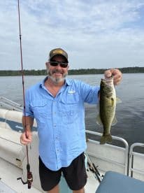 An angler proudly displaying a large Largemouth Bass while fishing on a pontoon boat in a serene lake setting.