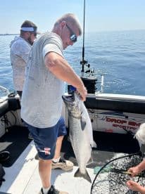 An angler proudly displaying a large Salmon while fishing on a charter boat in calm waters.