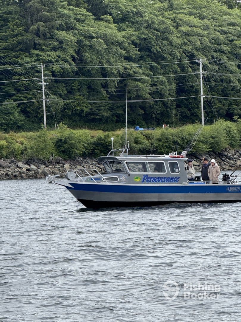 The fishing charter boat 'Perseverance' is seen on the water, surrounded by lush greenery, showcasing its sturdy design and fishing gear.