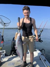 An angler proudly displaying a large Catfish while fishing on a sunny day, showcasing a successful catch on a boat.