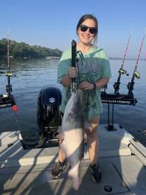 An angler proudly displaying a large Catfish while fishing on a serene lake, showcasing a beautiful day on the water.