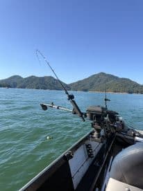 Interior view of a fishing boat showcasing the helm and rod holders, set against a backdrop of serene mountains and clear water.