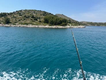 A scenic view of a fishing spot with a fishing rod pointing towards a rocky island in clear blue waters.
