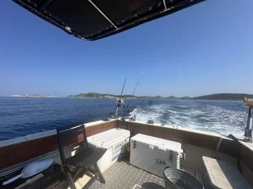 Interior view of a fishing boat showcasing seating and fishing gear, with a scenic backdrop of islands in the distance.