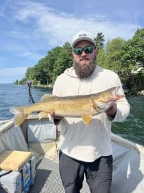 Angler proudly displaying a large Walleye while fishing on a scenic lake, showcasing a beautiful summer day.