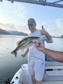 An angler proudly displays a large Largemouth Bass while fishing on a serene lake, showcasing a successful catch during a morning outing.
