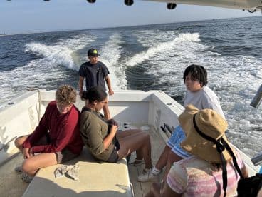 Group of young anglers relaxing inside a boat while cruising through calm waters, showcasing a comfortable fishing environment.