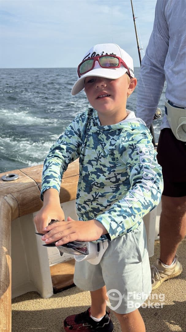A young angler actively reeling in a fish aboard a fishing boat, showcasing the excitement of fishing on the open water.