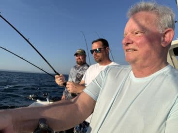 Three anglers engaged in fishing on a boat, with rods in hand, enjoying a sunny day on the water.